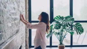 A square digital smart thermostat mounted on a living room wall